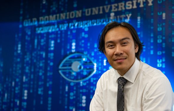 A student sits in front of the "School of Cybersecurity" sign at Old Dominion University.