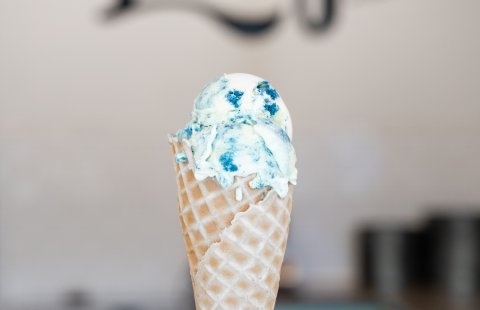 A hand holds a waffle cone with blue ice cream.