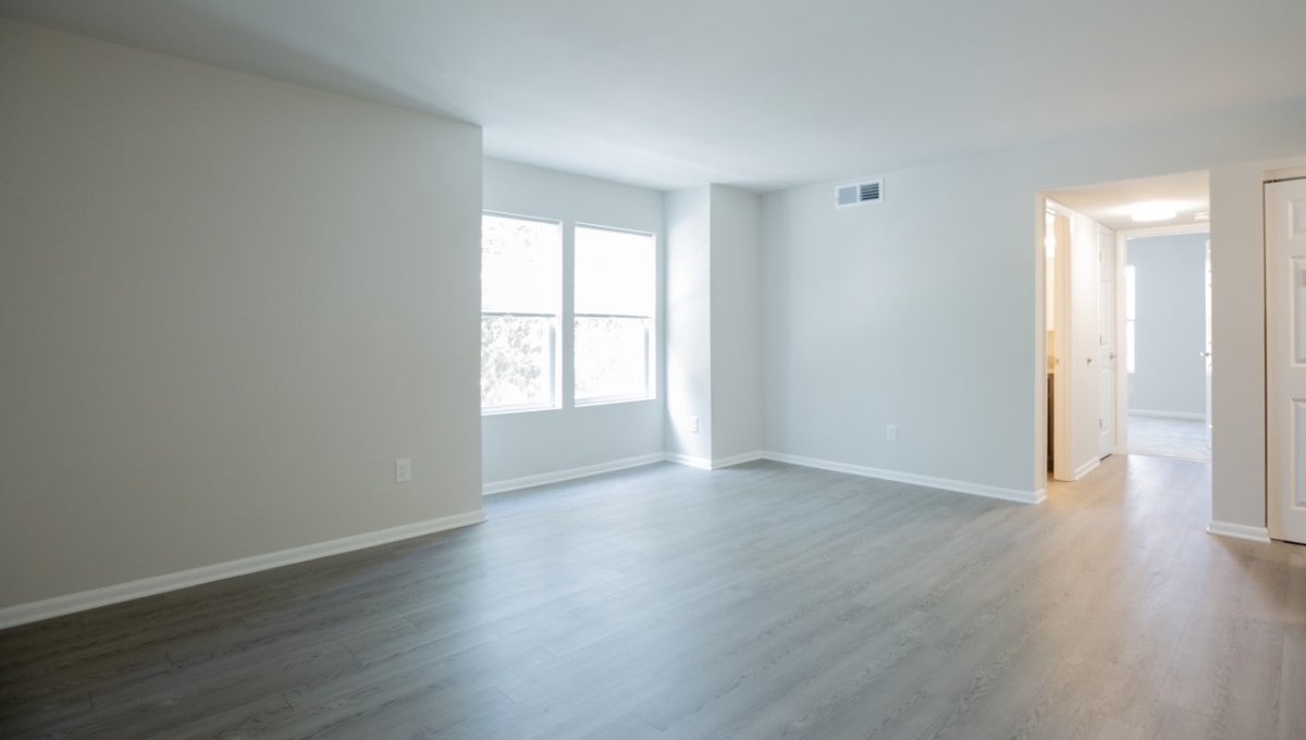 Unfurnished living room area with window and hall leading to other rooms.