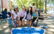 Students kneel in front of a painted crown on a sidewalk. 