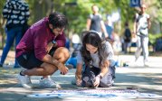 Two students paint a crown on a sidewalk on ODU's campus. 