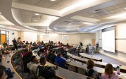 A group of students listen to a man speak at a podium in an auditorium.