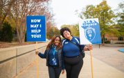 Two women hold signs while standing on a sidewalk on ODU's campus.