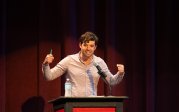 A man raises his arms while talking from a podium.