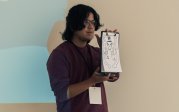 A student holds up a design on a whiteboard.