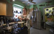 A woman stands in front of a stove tending to a boiling pot. 