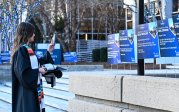 A woman in a graduation gown takes photos of yard signs. 