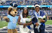 ODU's mascot stands next to two students on the football field. 