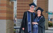 Two smiling people in graduation caps and robes stand outside of Chartway arena in December 2025.