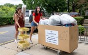 A pair of students push a cart full of items into their dorm.