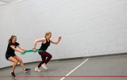 A woman holds resistance bands while another woman runs forward.