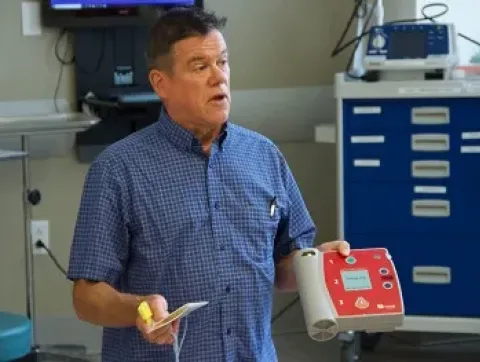 A man instructs a class while holding an AED.