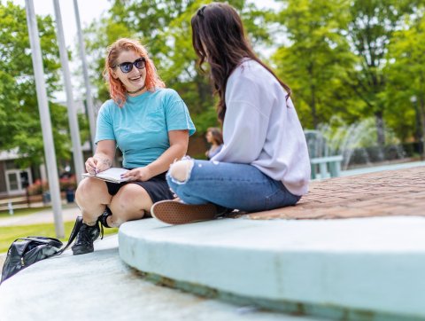 Two female students are sitting on the steps in front of the Webb center talking