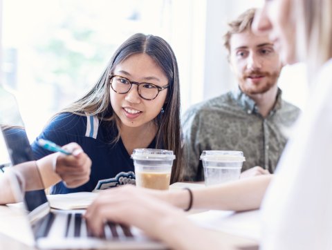 Three students are sitting around a laptop studying