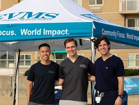 Three men wearing dark surgical scrubs smile at the camera w