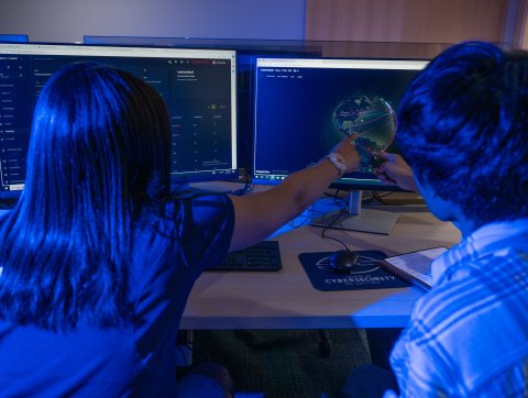 Two students in a computer lab look at an image of a global map.