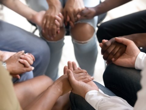 Diverse people sitting in circle holding hands at group therapy.