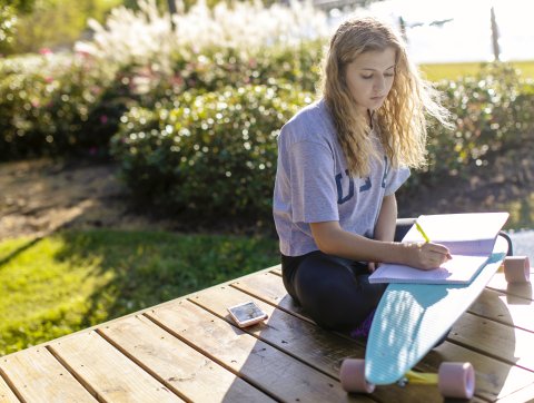 Student sits outside writing on notebook