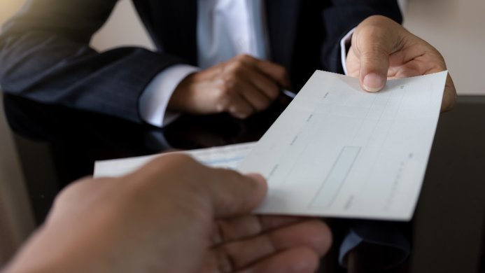 Business woman in a suit holds a pen while giving a bank check to colleague with checkbook on the desk at office.