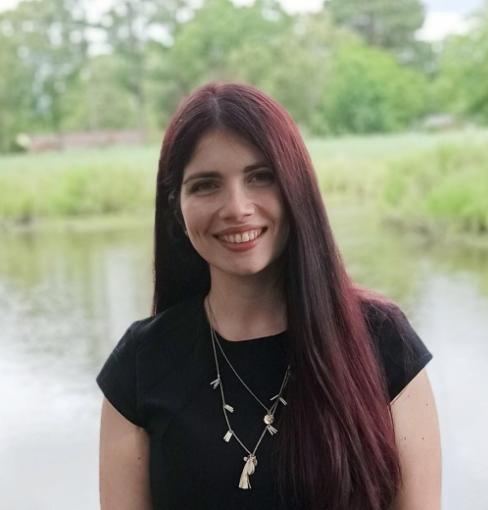 Olga Karadimou is standing in front of a pond with long dark brown hair with red streaks