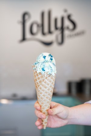A hand holds a waffle cone with blue ice cream.