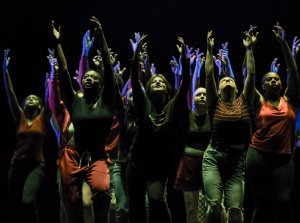 student dancers on a dark stage with arms raised overhead