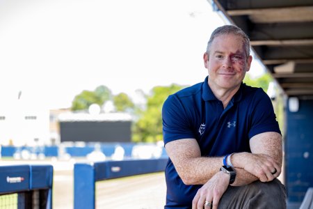 A man in a blue shirt stands in a baseball dugout 