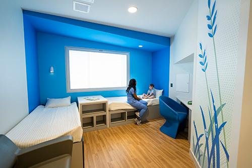 A female therapist in blue medical scrubs sits on a bed in a
