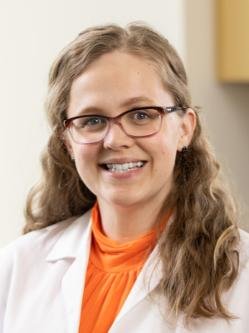 Dr. Blumrick has long wavy blonde hair, is wearing glasses a
