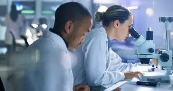 Two students in profile, one looking through a microscope